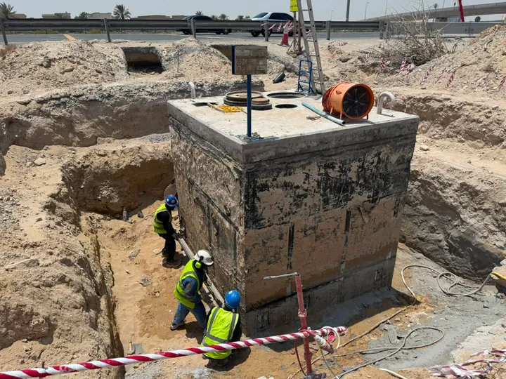 An exposed concrete chamber with cutting equipment and site workers beside an excavation