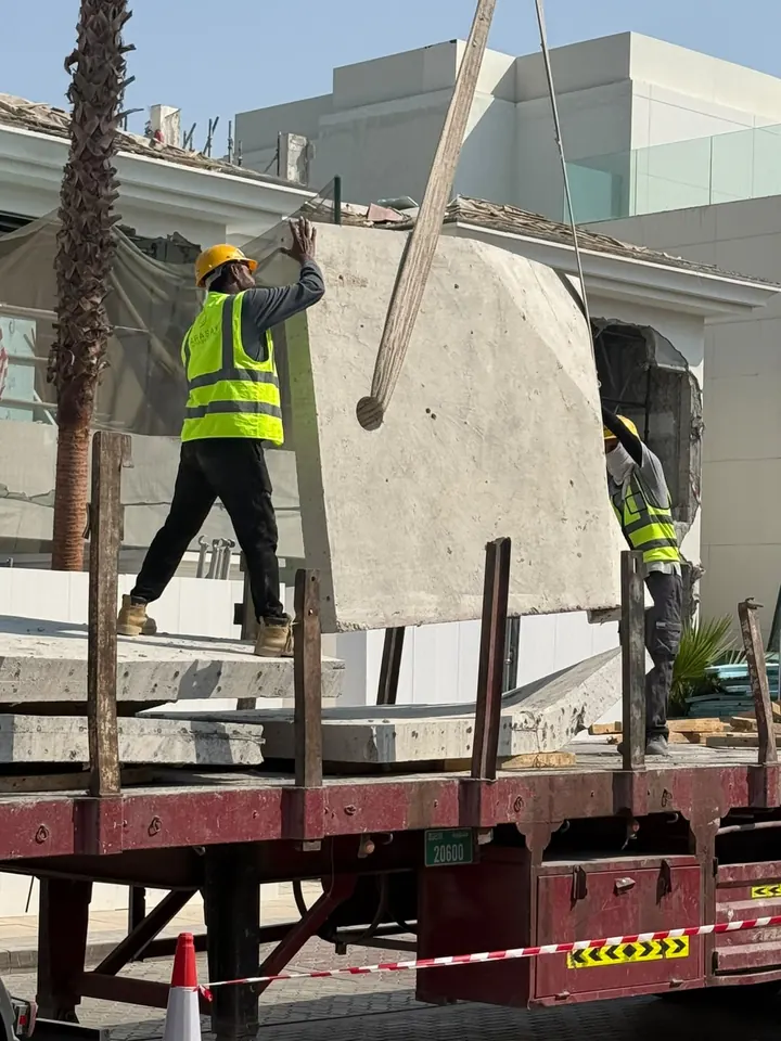 Arasar workers guiding a large concrete panel suspended by lifting slings above a truck bed
