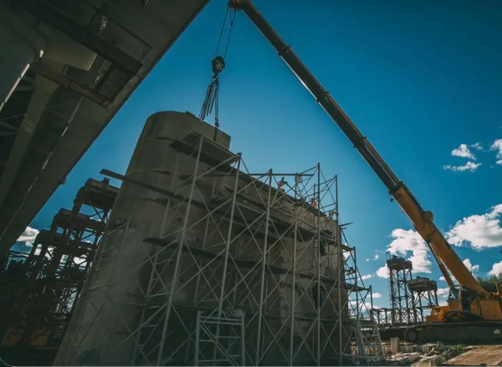 A crane lifting a section from a cylindrical concrete structure surrounded by scaffolding