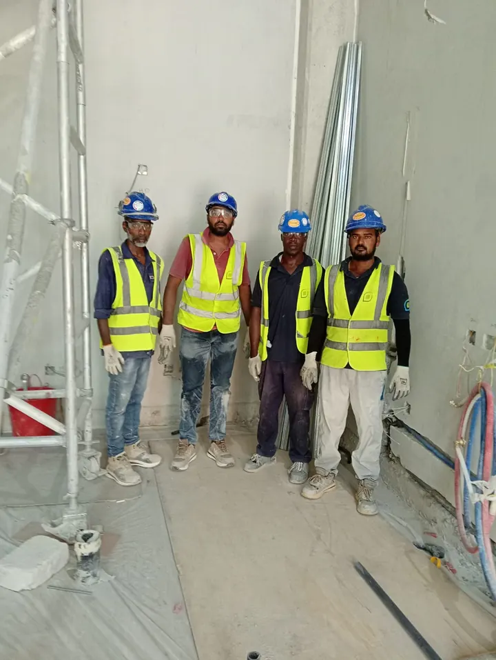 Four Arasar site workers wearing hard hats and high-visibility vests beside interior scaffolding